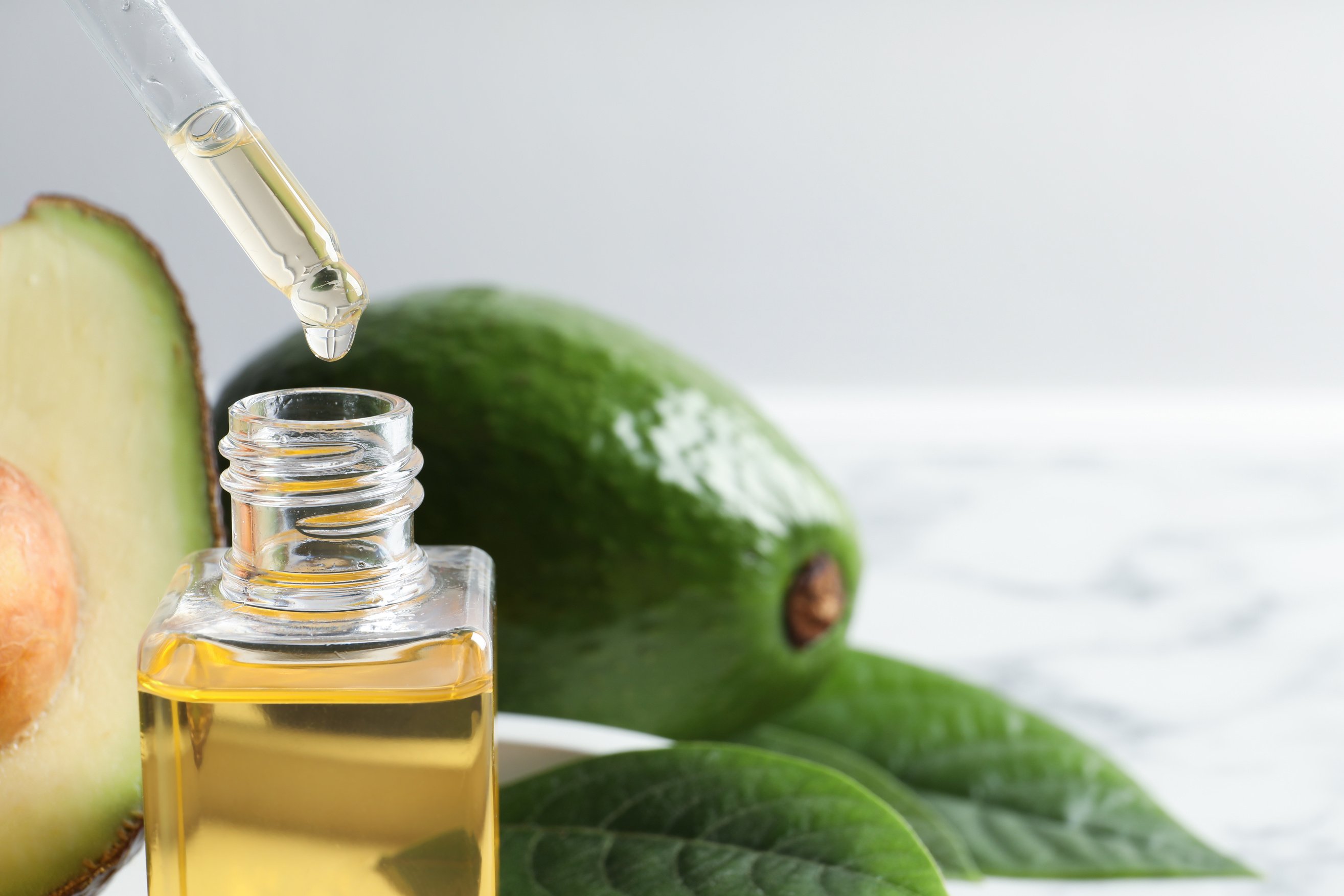 Dripping Avocado Essential Oil into Bottle on Table, Closeup. Space for Text